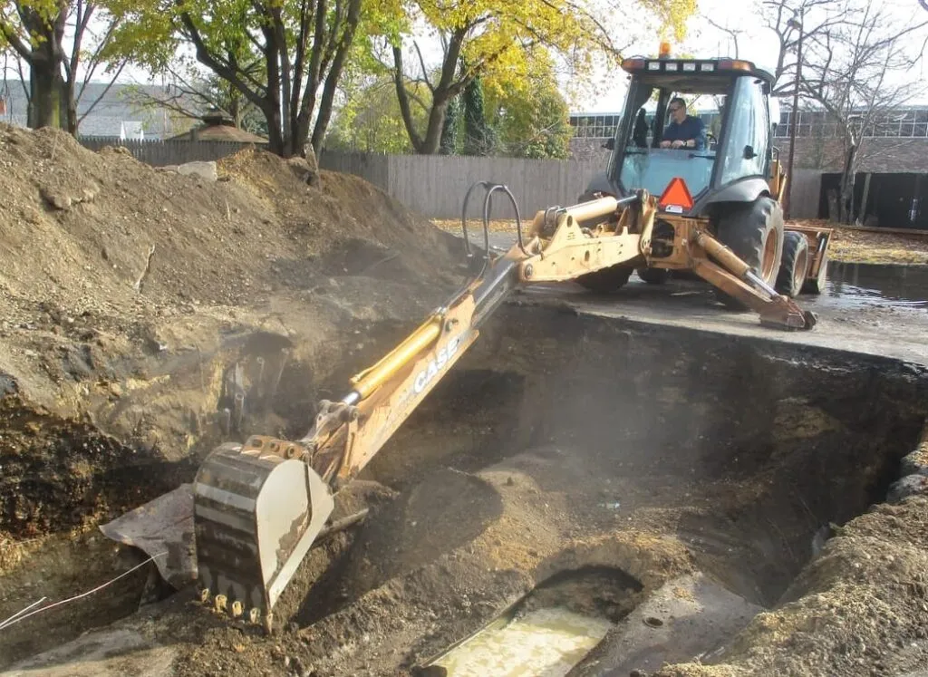 Case backhoe excavating a large open pit on a wooded lot in autumn