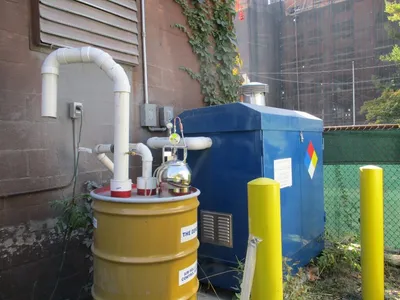 Outdoor vapor extraction system with blue enclosure, PVC piping, and carbon drum