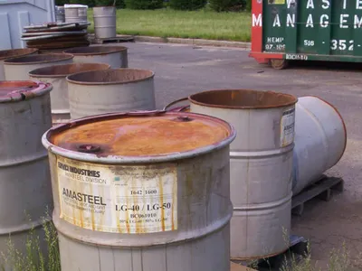 Rusted steel drums staged beside a green Waste Management roll-off dumpster outdoors