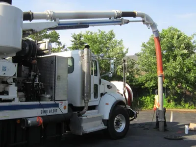 Vacuum truck extending a suction hose to a worker cleaning a drywell in a parking lot