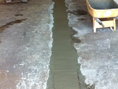 Fresh grout filling a trench across a stained warehouse concrete floor