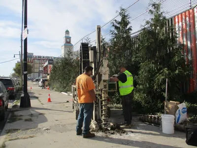 Two workers running a sidewalk-mounted soil boring rig on a city street