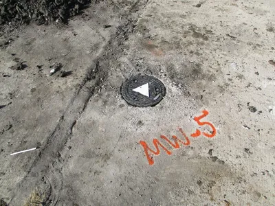 Flush-mount monitoring well cover set in pavement marked MW-5 in orange paint