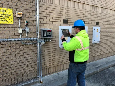 Technician inspecting a wall-mounted overfill alarm panel with a tablet