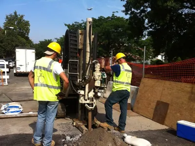 Two G.C. Environmental crew in hi-vis vests operating a direct-push Geoprobe rig curbside
