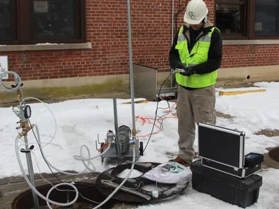 Technician running a tank tightness test rig with a pressure gauge in snow