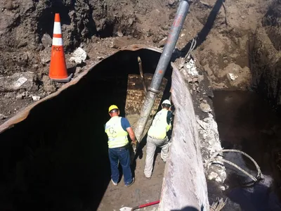 Two technicians in hi-vis gear entering a large excavated tank for cleaning
