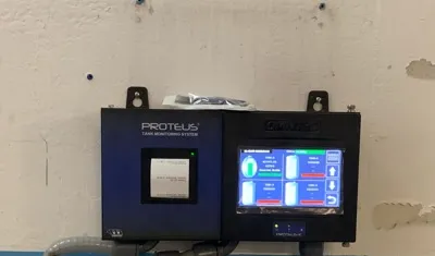 Proteus tank-monitoring console beside a touchscreen control unit on a wall