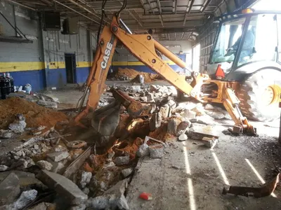 CASE backhoe breaking up a garage floor slab to reach a buried hydraulic lift