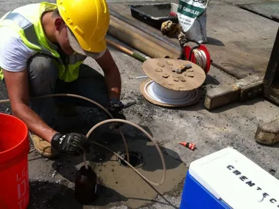 Worker in hard hat sampling groundwater into an amber bottle at a flush-mount well