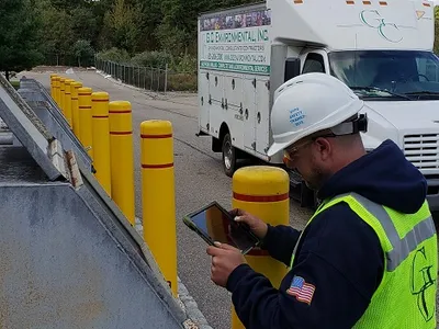 Inspector with a tablet checking bollards by a flammable liquids tank rack