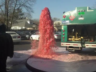 Vacuum tanker truck flushing a manhole as pink water erupts over foamy pavement