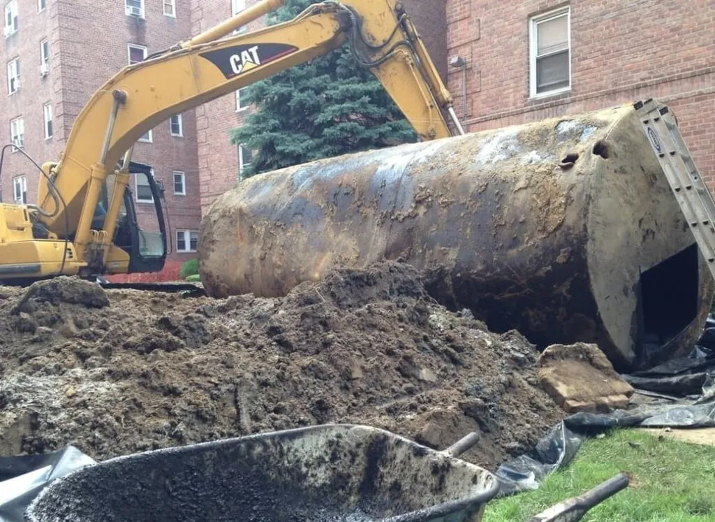Rusty steel underground tank pulled from a pit beside a brick apartment building