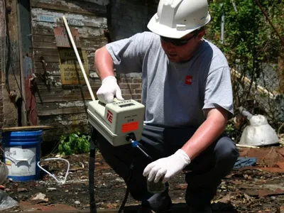 Technician screening a soil sample with a handheld organic vapor meter at a derelict site