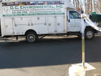Yellow groundwater sample tube held over a bucket beside a G.C. Environmental service truck