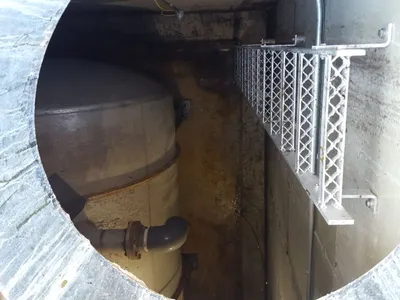 View down an open manway into a tank vault with piping and an aluminum ladder