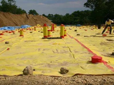 Yellow vapor-barrier membrane with red-capped vent risers across a prepared building pad