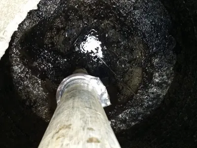 Vacuum hose nozzle removing black sludge from inside a concrete drywell