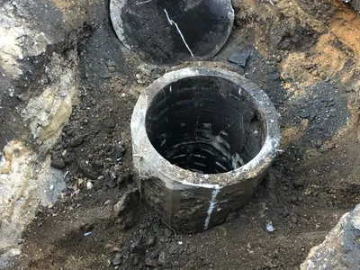 Excavated concrete dry well with its cracked cap lifted off, opening exposed