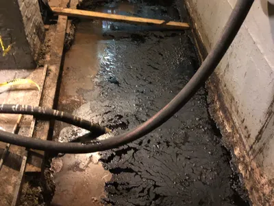 Suction hose draining black oily sludge from a flooded basement trench