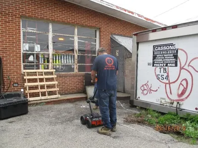 Worker scanning pavement with a ground-penetrating radar cart beside a storage trailer