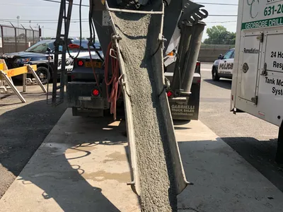 Concrete pouring from a mixer-truck chute into a sidewalk vault opening