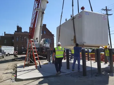 Crane setting a vaulted diesel tank as a crew guides it into place
