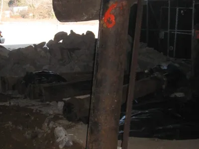 Rusty hydraulic lift cylinder being pulled from the ground by a backhoe