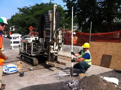 Track-mounted drill rig installing a groundwater monitoring well on a city street