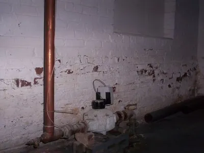 Peeling painted brick basement wall with an old gas meter and copper pipe
