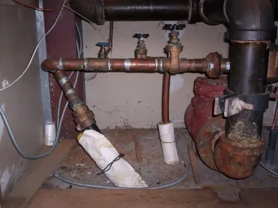 Basement plumbing with valves, a red pump, and an insulation-wrapped pipe section