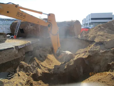 Excavator digging a tank pit beside removed tanks and a G.C. Environmental truck
