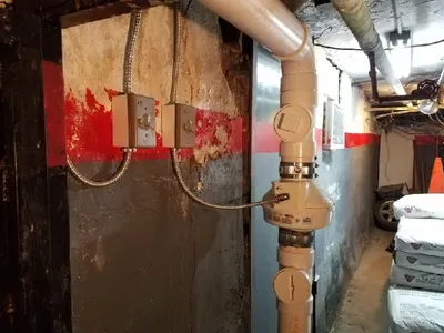 Sub-slab depressurization riser with an inline fan and control boxes in a basement