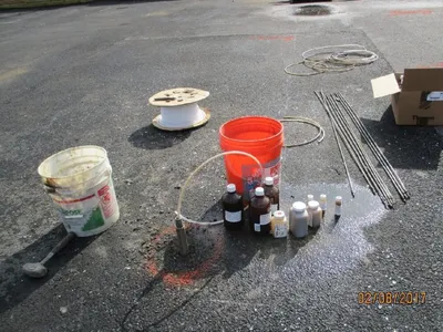 Amber sample bottles, buckets, and steel drive rods staged on pavement for sampling