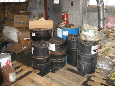 Black waste drums on wooden pallets inside a cluttered storage room