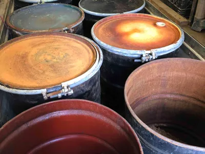 Rusted steel drums with one open revealing dark contaminated soil