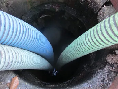 Flexible suction hoses inserted into a circular concrete drywell for cleaning