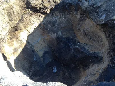 Open excavation pit with layered soil walls where a well was removed