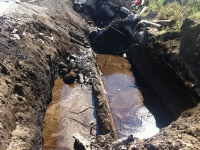 Petroleum-stained water pooling in an excavated trench around an exposed pipe