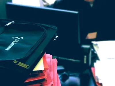 Stacked red record folders and a G.C. Environmental case beside a staffer at a computer
