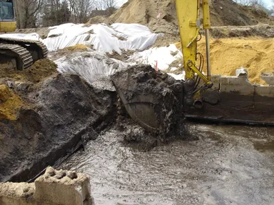 Open excavation holding green-stained groundwater next to a brick industrial building