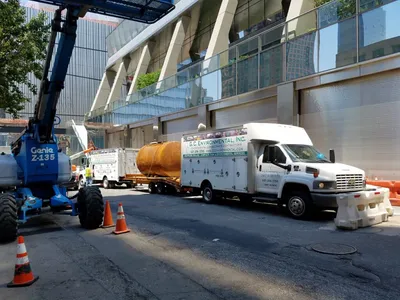 Rusty steel tank on a flatbed trailer beside a G.C. Environmental box truck