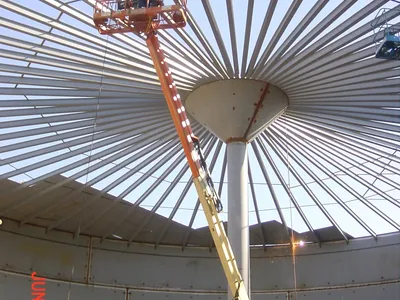 Worker on a boom lift assembling the domed roof framing of a large tank