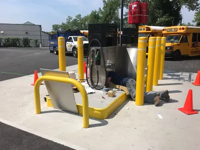 Technician servicing a fleet dispenser from the ground near parked school buses