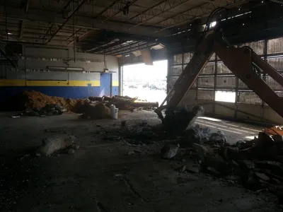 Backhoe demolishing a service-bay floor inside a garage to remove a lift