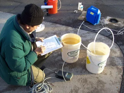 Field technician logging data beside groundwater purge buckets and a handheld meter