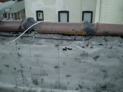 Cracked, alligatored paint coating on a rooftop pipe and parapet wall