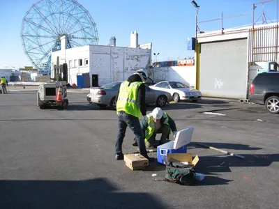 Two technicians packing soil samples into a cooler in a lot with a Ferris wheel behind