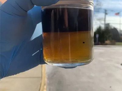 Gloved hand holding a sample jar showing dark contamination layered over amber fuel
