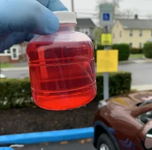 Gloved hand holding a sample bottle of bright red dyed fuel